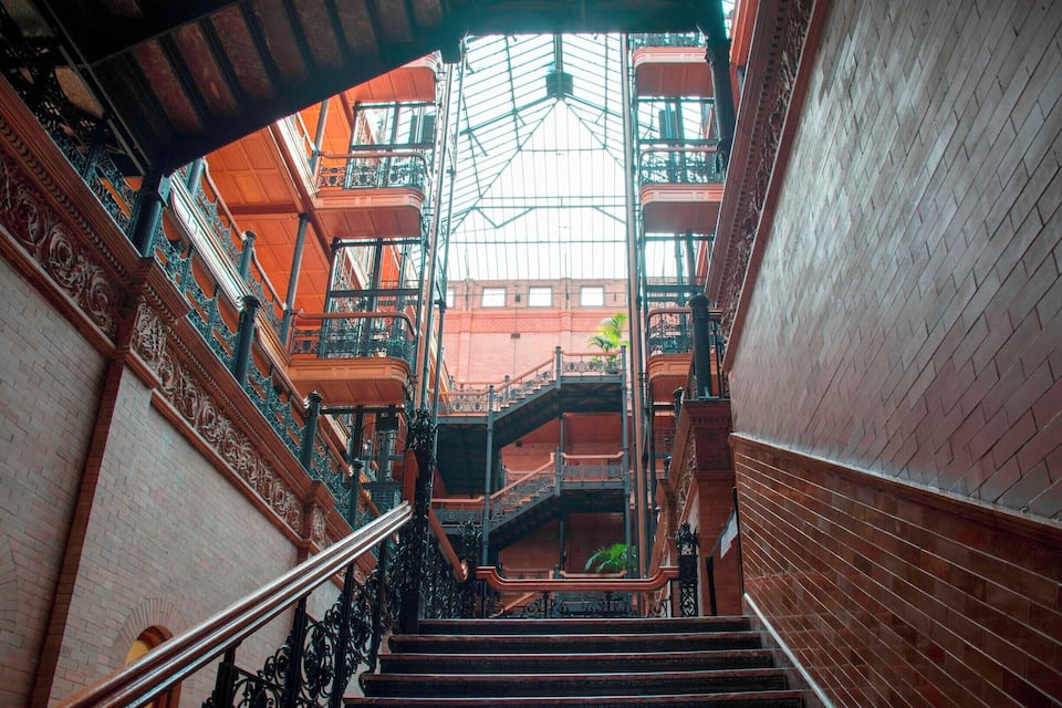 Uma escadaria imponente com grades de ferro ornamentadas e teto de vidro.
