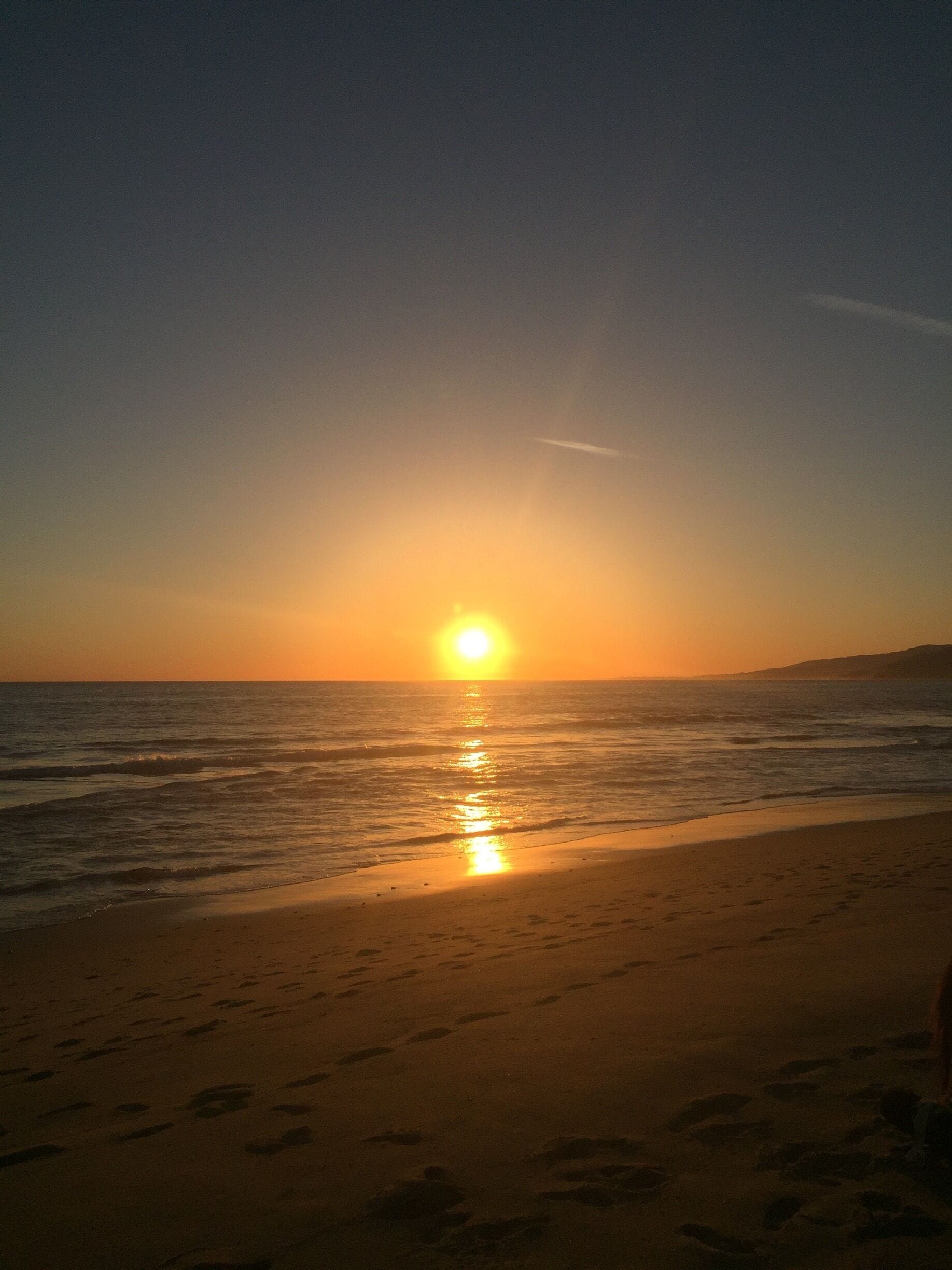 A sunset over a beach with footprints in the sand.