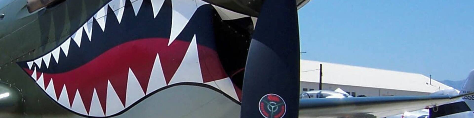 A vintage aircraft with a shark mouth decal on its nose.