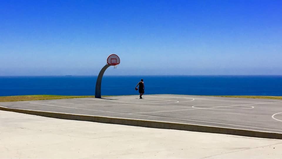 A basketball court with a hoop overlooking the ocean.