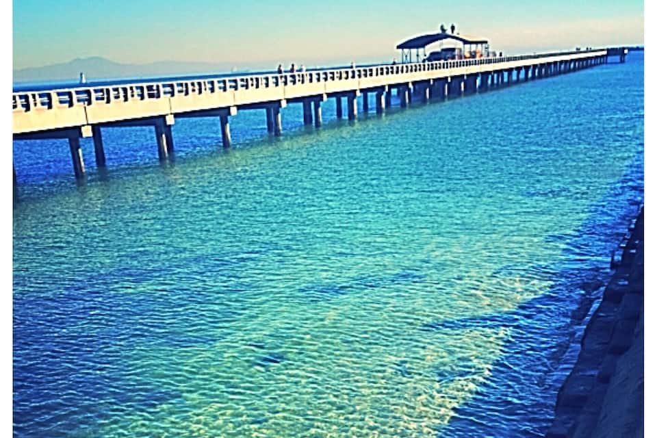 A pier extending into a clear blue sea with a rocky shoreline.