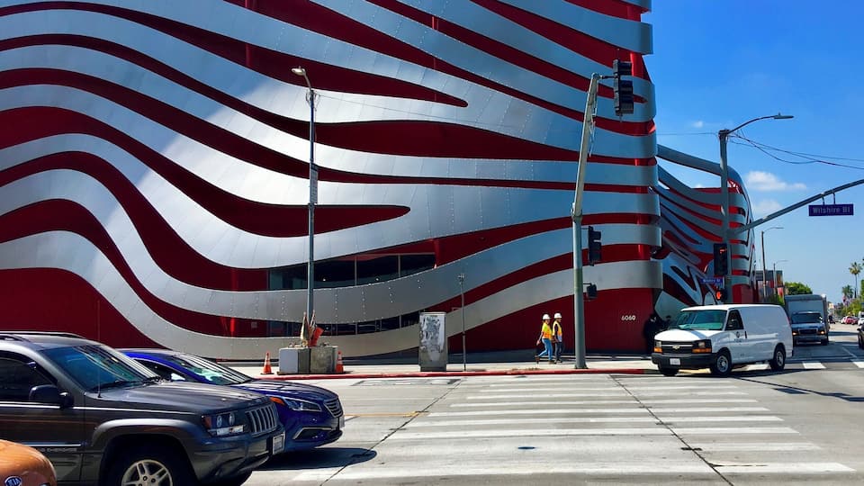 Ein modernes Gebäude mit einer gewellten roten und weißen Fassade, einer Fußgängerquerung und Autos an einer Ampel.