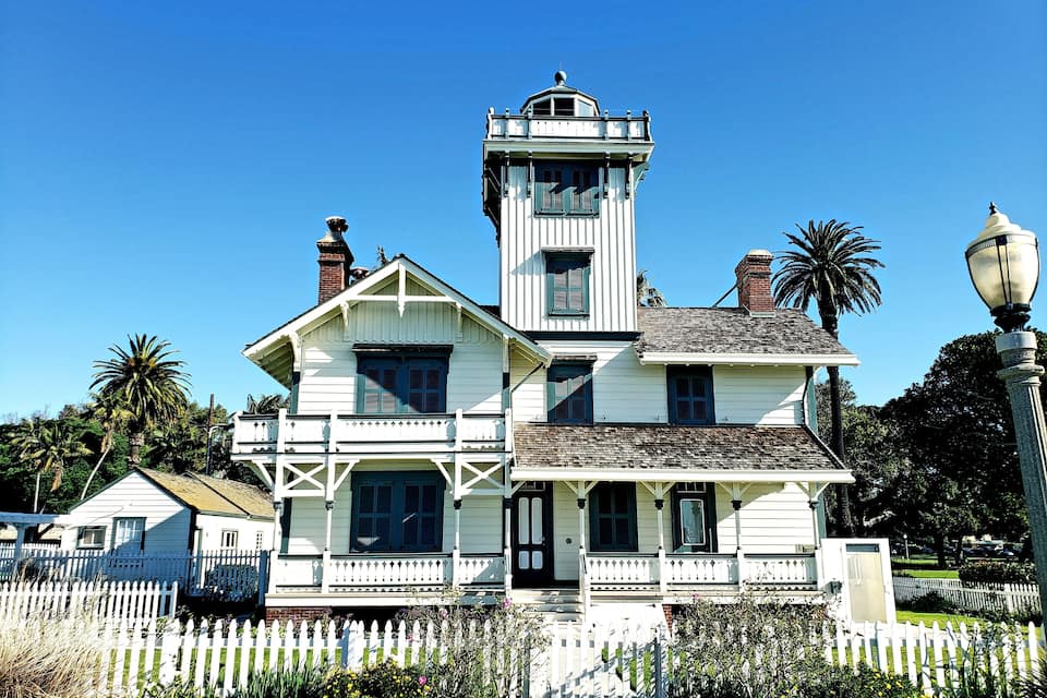 A white Victorian-style house with a tower and a white picket fence.