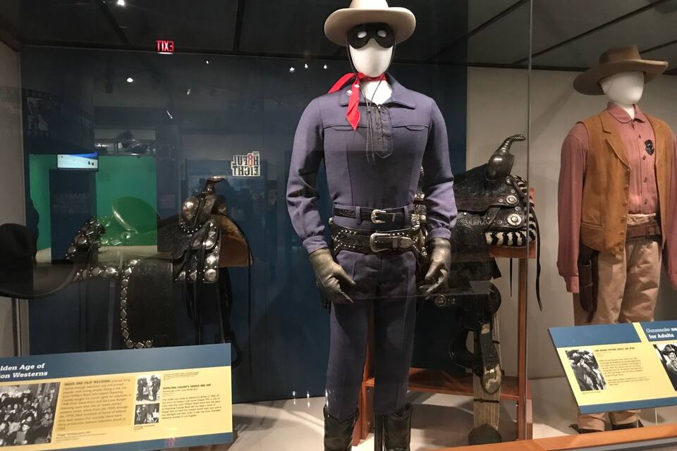 A museum exhibit with mannequins dressed in western attire, including cowboy hats and boots.