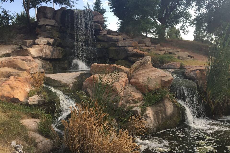 A waterfall cascading over rocks into a pond surrounded by grass and trees.