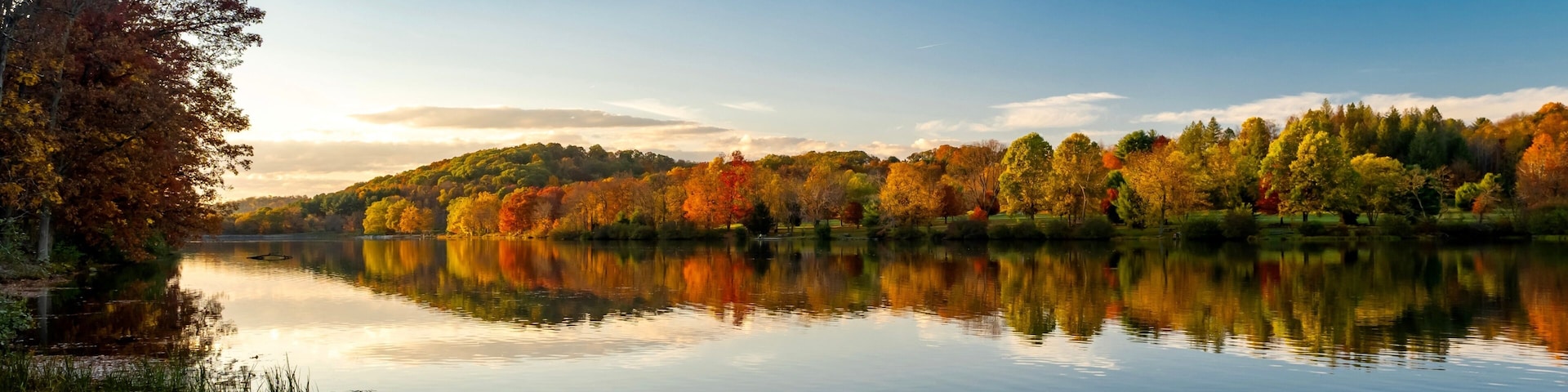 A calm lake with autumn foliage, a clear sky, and a distant hill.