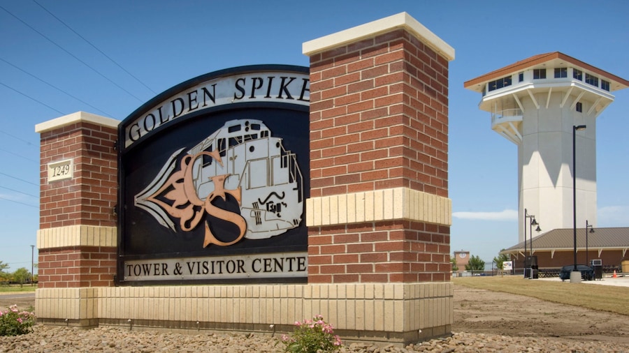 A sign for the Golden Spike Tower & Visitor Center with a brick building and a tower in the background.