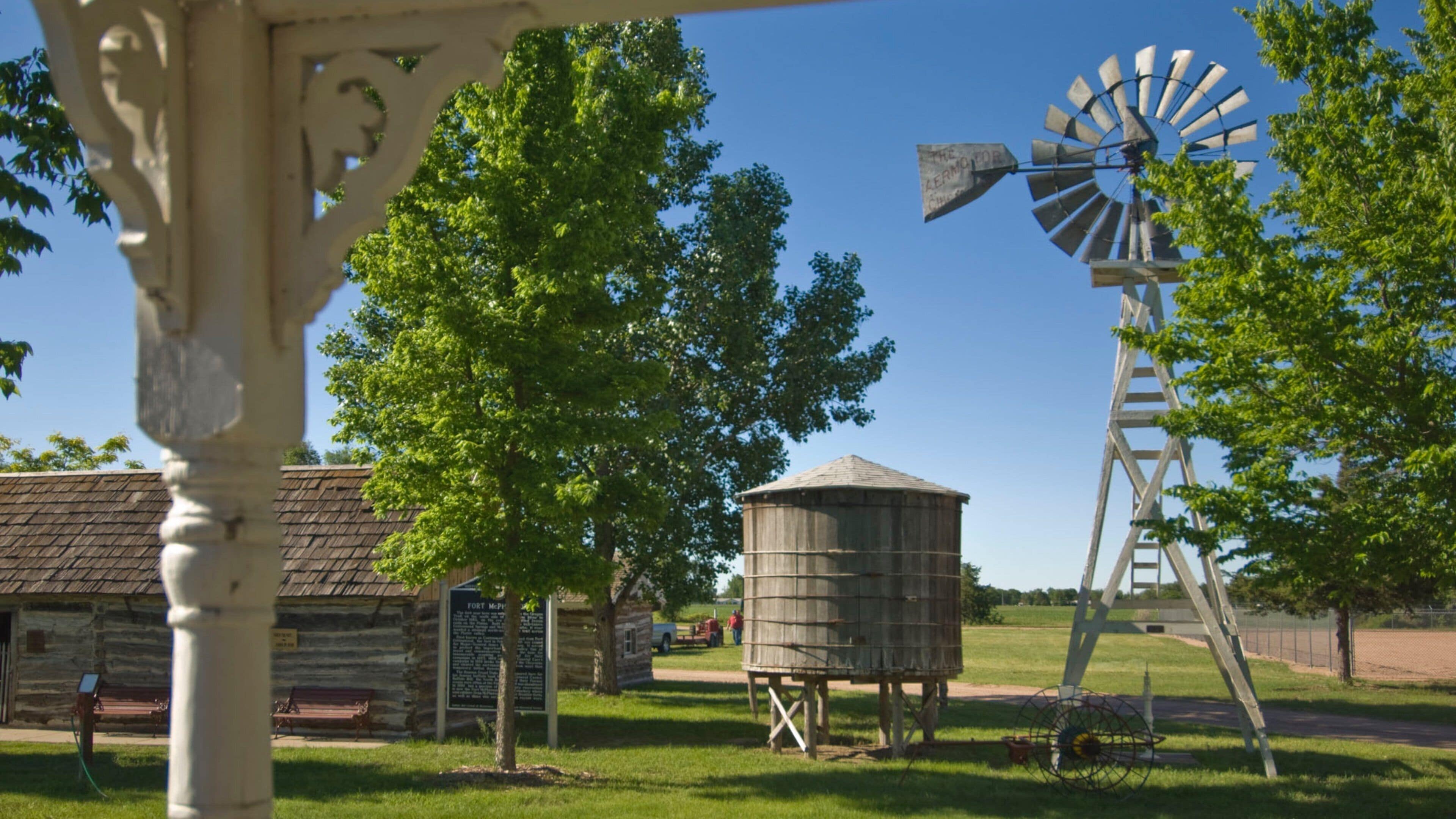 A windmill, wooden water tower, and rustic buildings in a park.