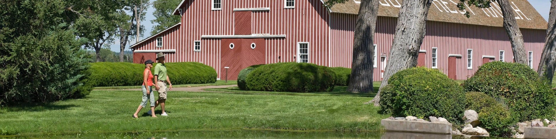 A red barn with a pond in front, surrounded by trees and greenery.