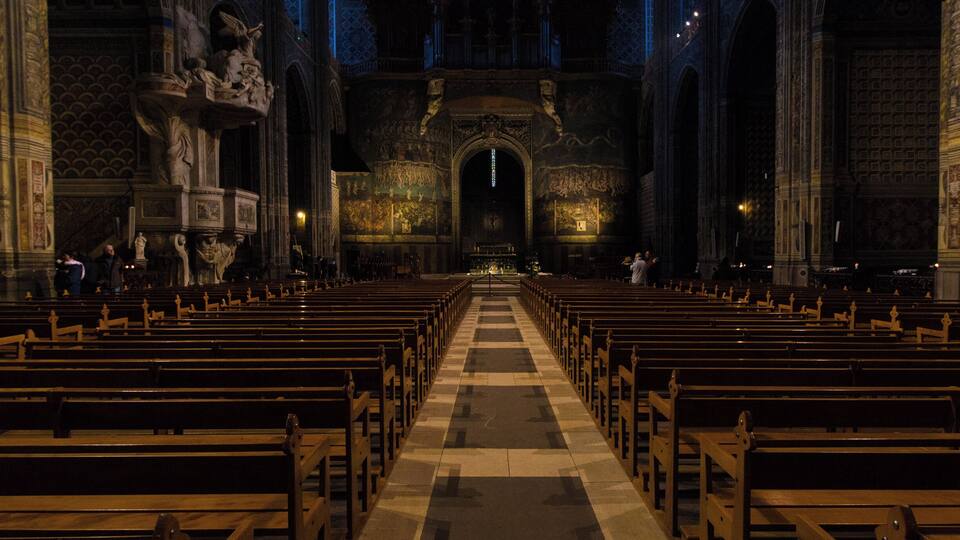 An interior of a church with rows of wooden pews, statues, and an ornate altar.