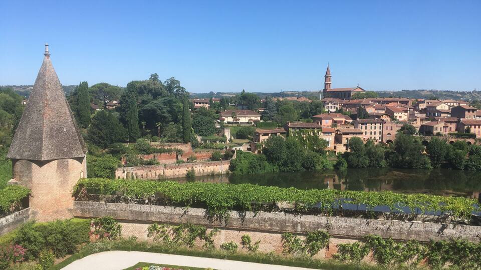 A historic town with a prominent tower, a river, and well-maintained gardens.