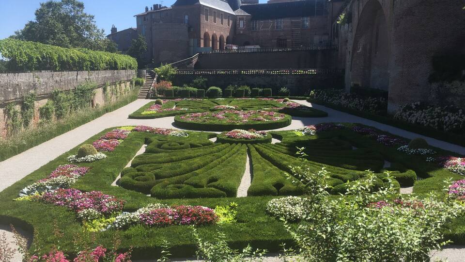 A meticulously landscaped garden with geometric flower beds and a historic building in the background.