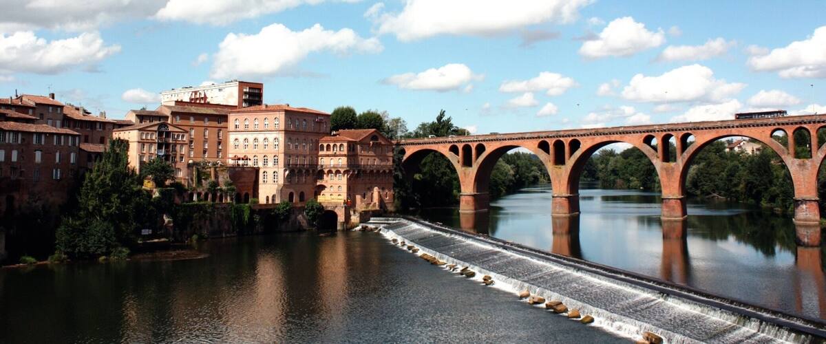 A river with a bridge, buildings, and a clear sky.