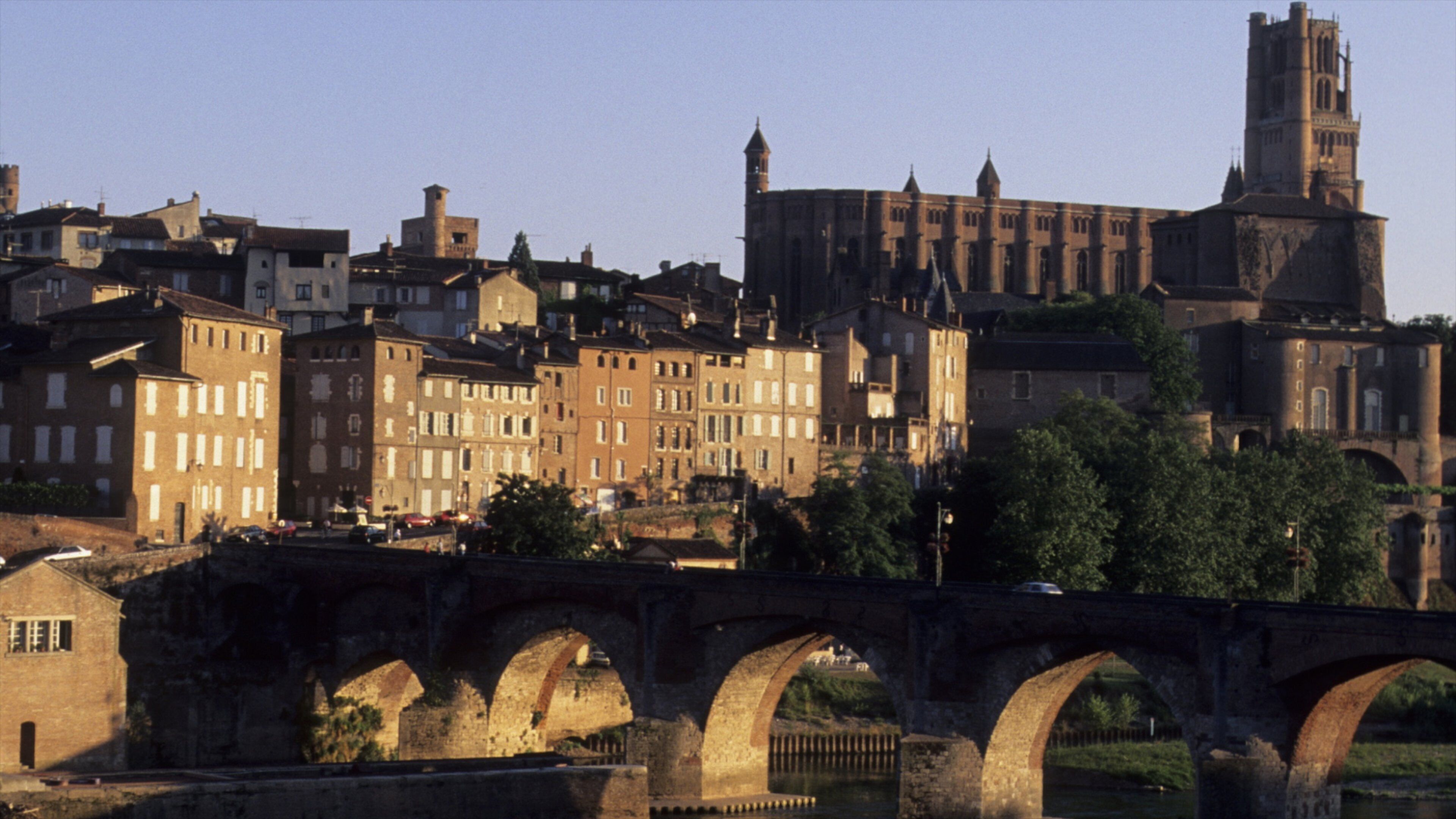 A historic bridge with multiple arches spanning a river, surrounded by a mix of residential and religious buildings.