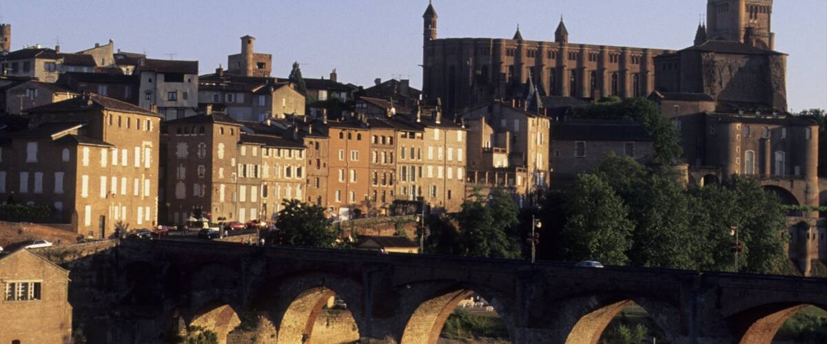 A historic bridge with multiple arches spanning a river, surrounded by a mix of residential and religious buildings.