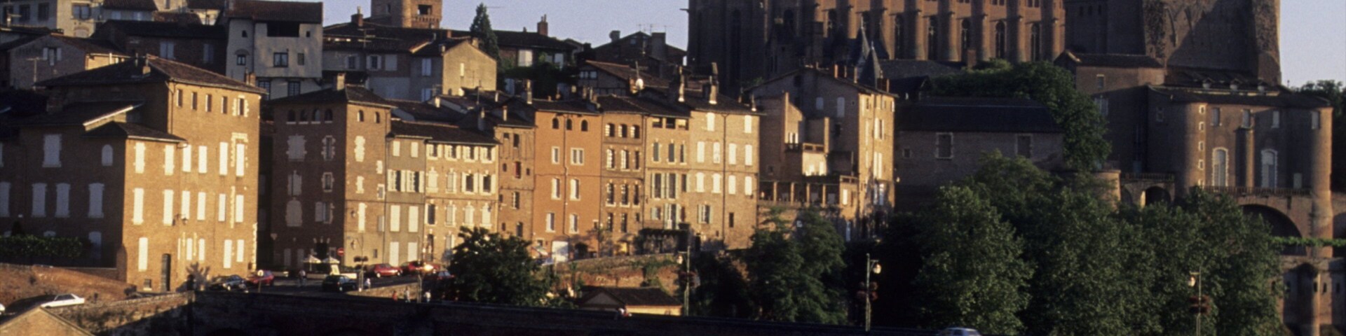 A historic bridge with multiple arches spanning a river, surrounded by a mix of residential and religious buildings.