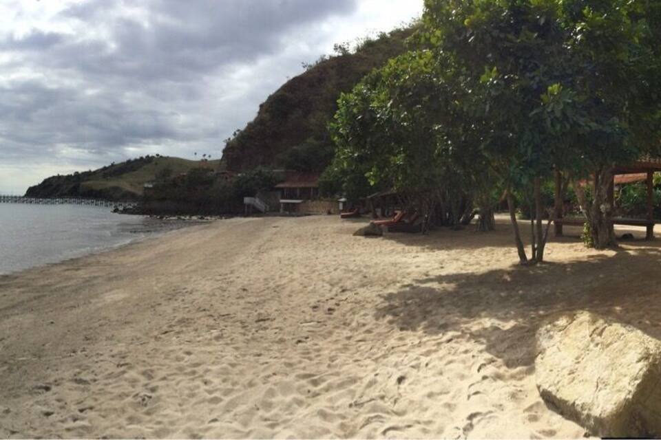 Una playa arenosa con aguas tranquilas, una isla distante y un cielo nublado.