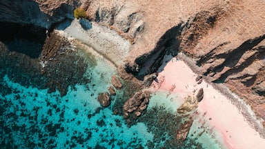 Vista aérea de uma paisagem costeira com águas turquesa cristalinas, formações rochosas e uma praia de areia rosa.