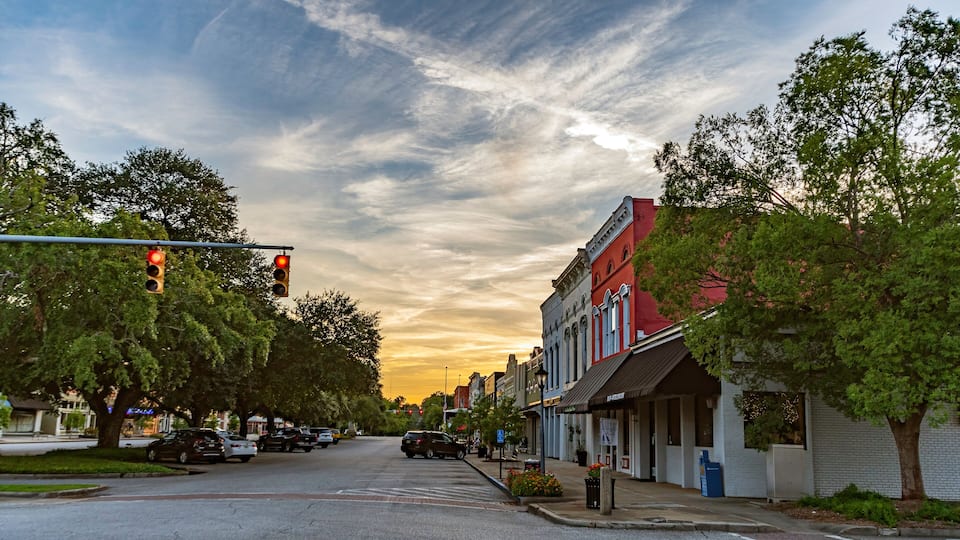 A street with a traffic light, parked cars, and buildings with storefronts.