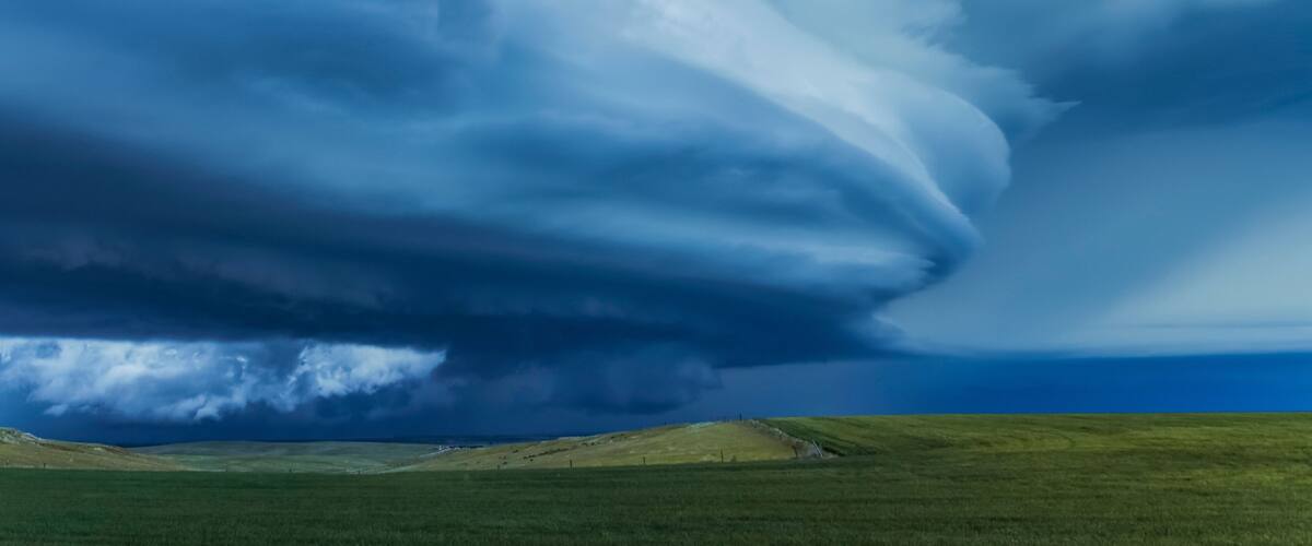 A vast landscape with rolling green hills and a dramatic sky featuring a large, swirling cloud formation.