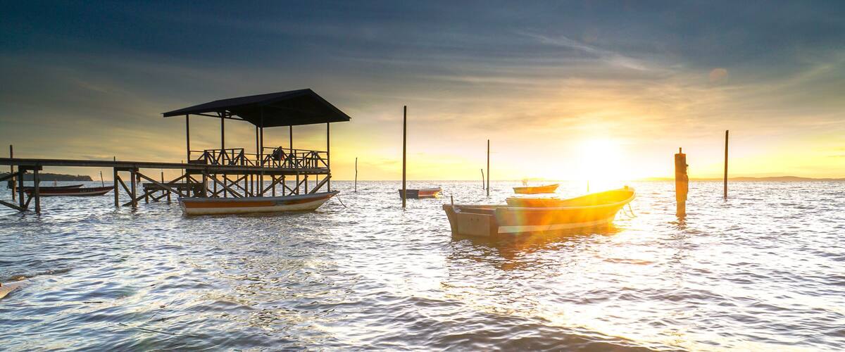 A pier with a covered seating area and a boat docked at sunset.