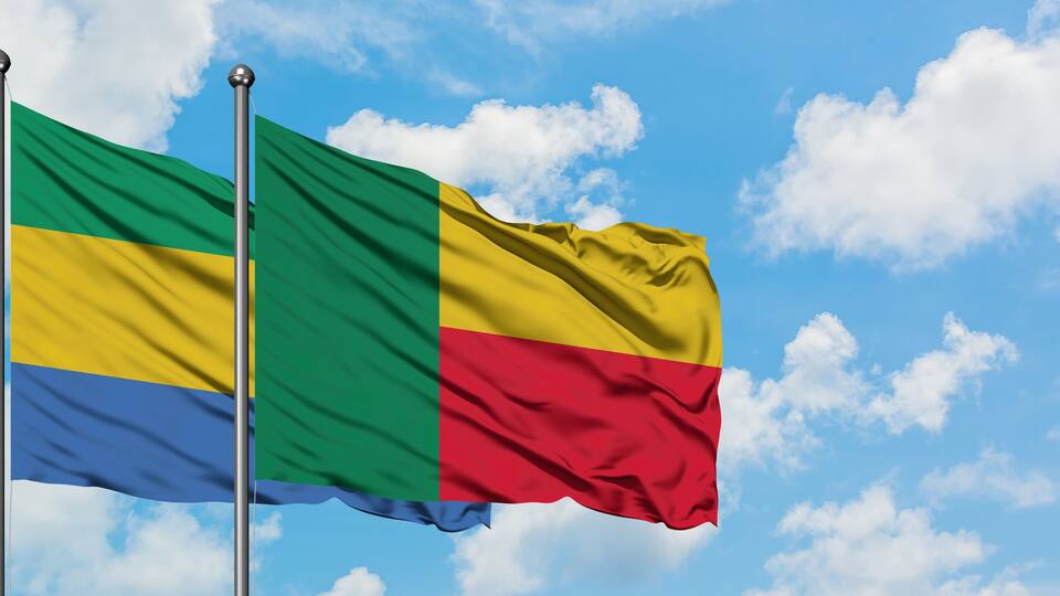 Two flags on flagpoles against a blue sky with clouds.