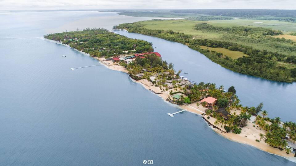 An aerial view of a coastal area with a beach, buildings, and a forested peninsula.