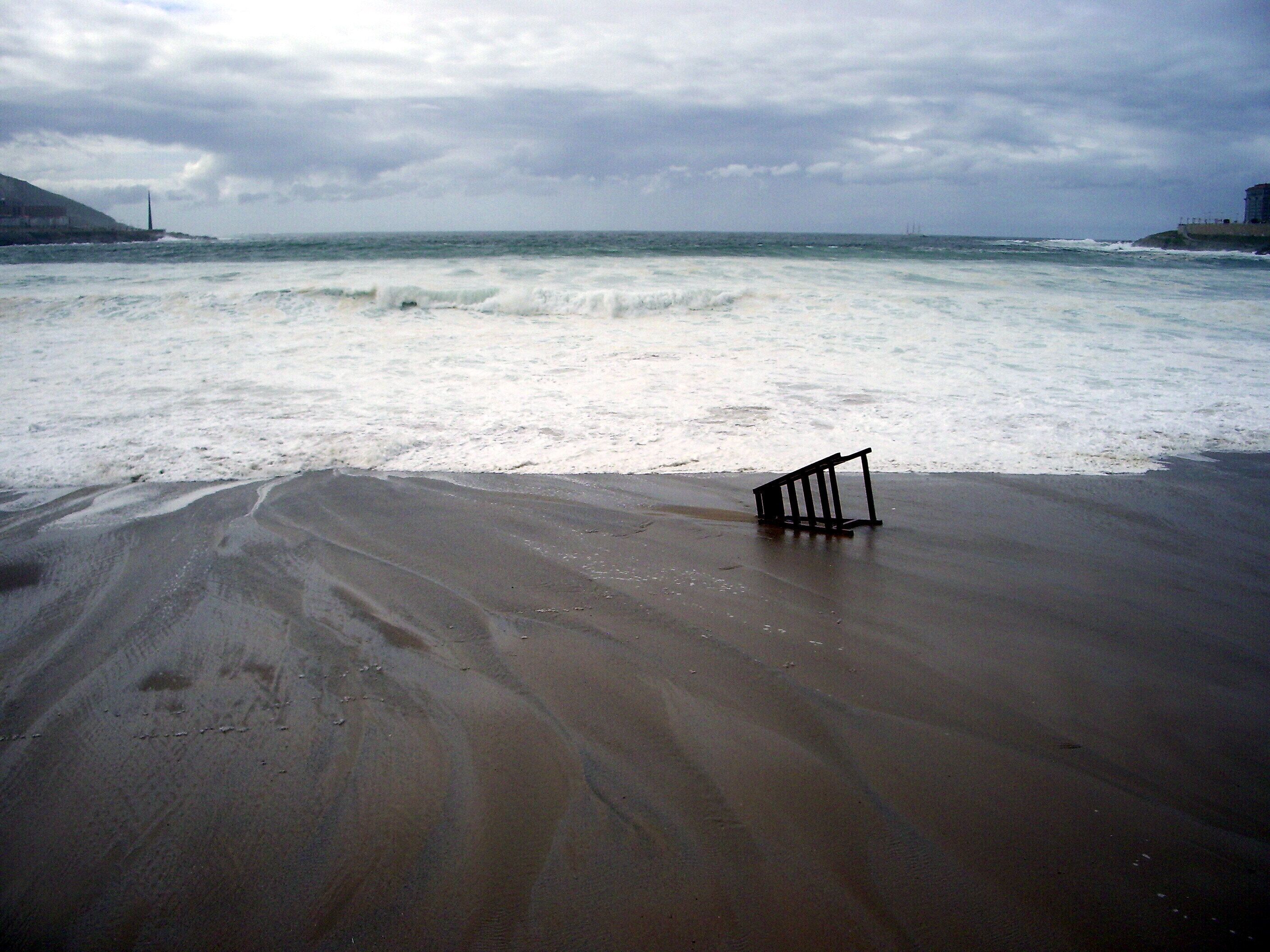 A beach with rough waves and a black metal structure on the sand.