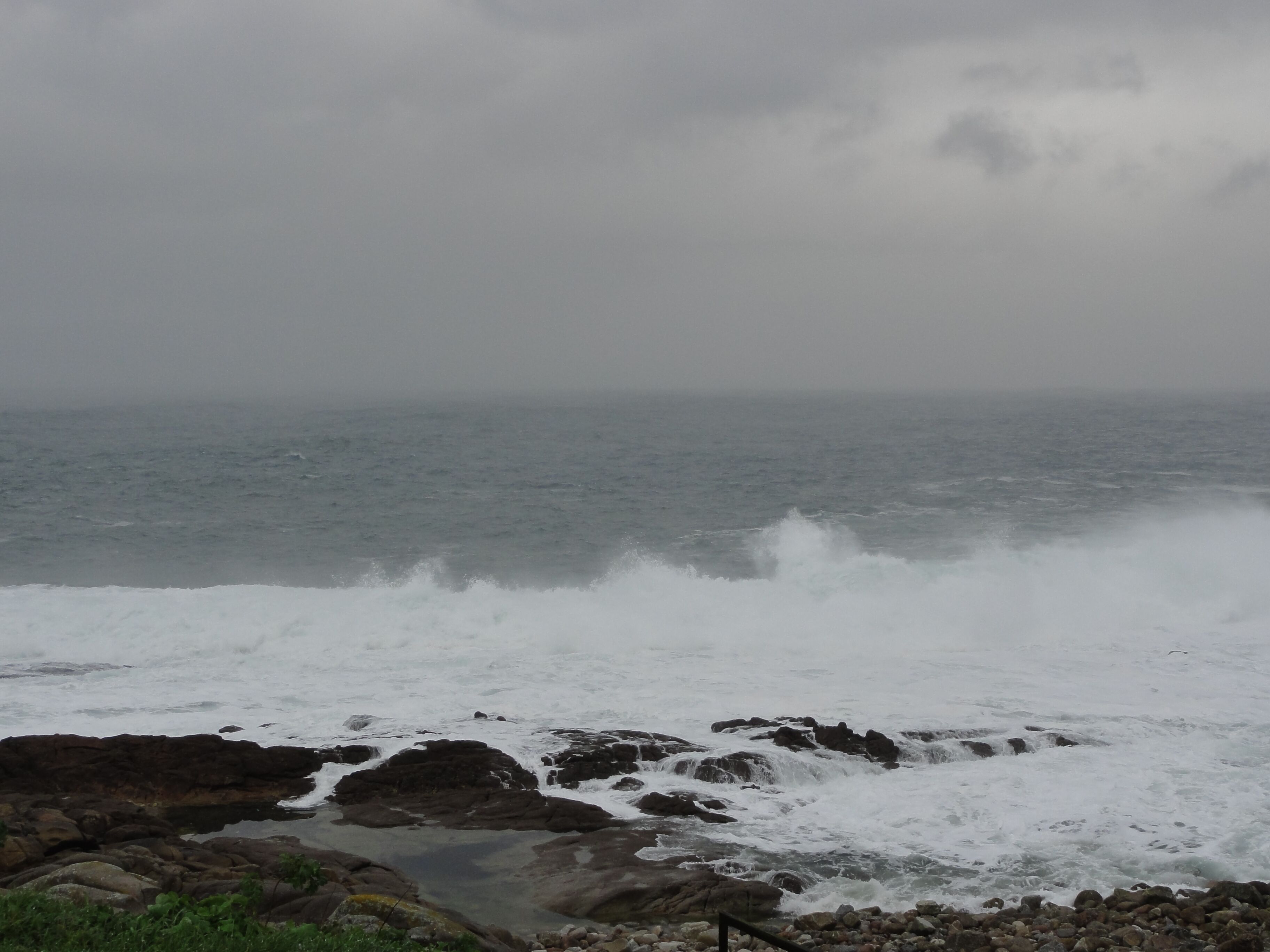 A rocky shoreline with waves crashing against the rocks under an overcast sky.