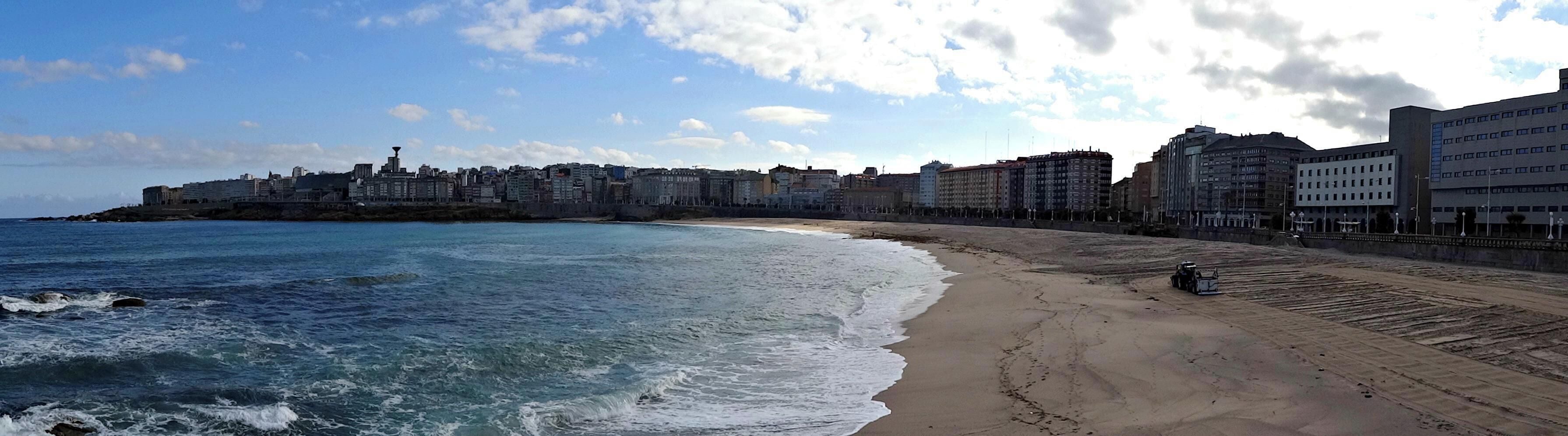 A coastal cityscape with a beach, ocean waves, and a variety of buildings.