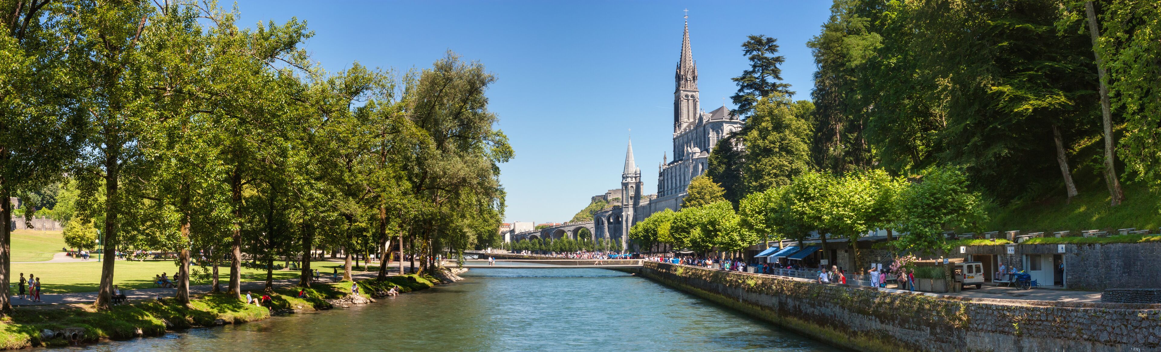 A river with a stone bridge, trees, and a historic building with a tall spire.