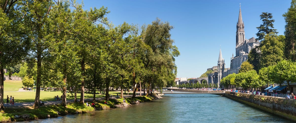A river with a stone bridge, trees, and a historic building with a tall spire.