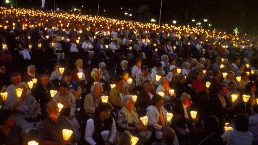 Lourdes que inclui cenas noturnas e arte performática assim como um grande grupo de pessoas