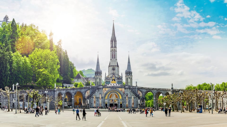 A historic cathedral with a tall spire, surrounded by a park with statues and trees.