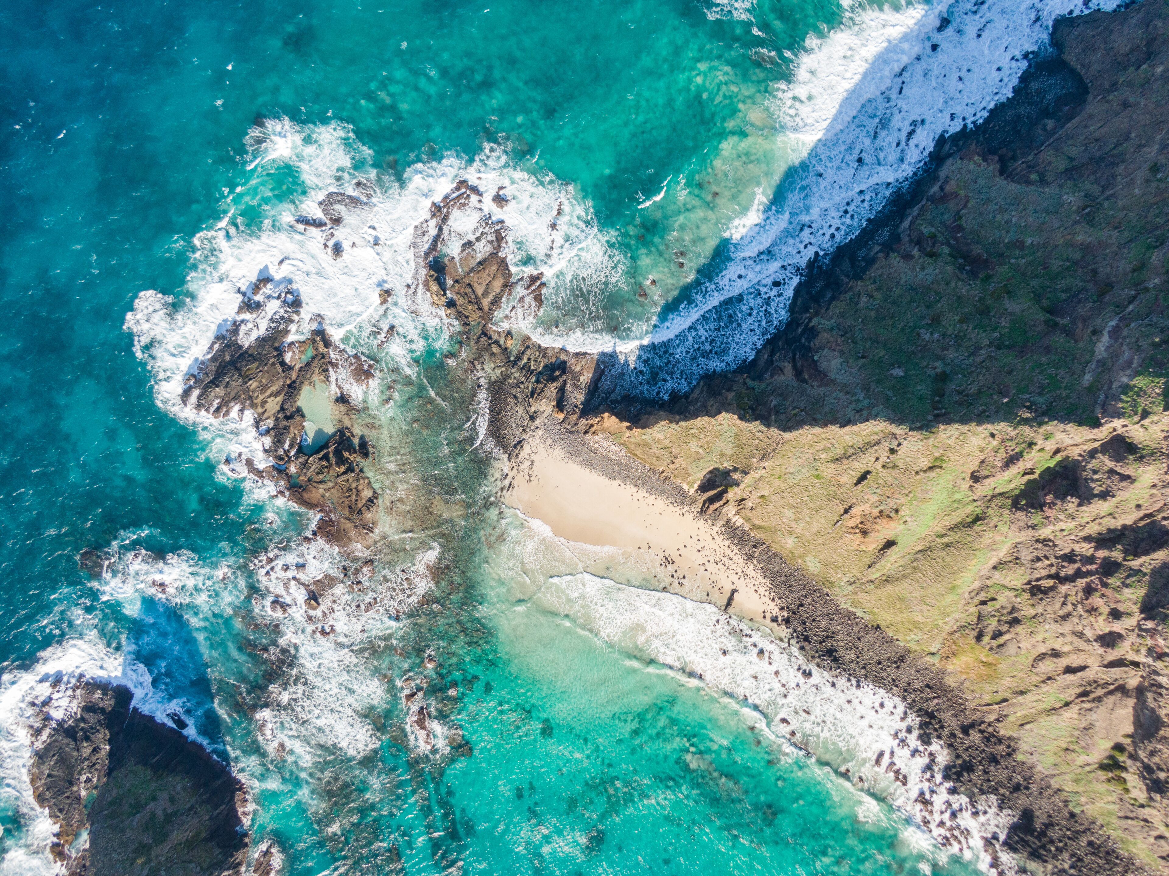 A coastal landscape with turquoise waters, rocky cliffs, and a sandy beach.