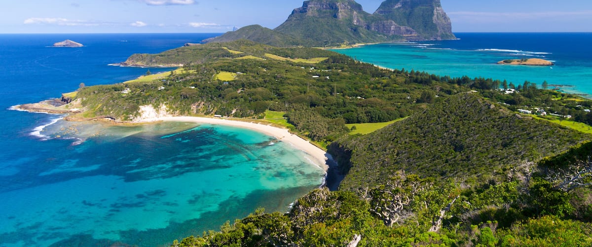 A coastal landscape with a prominent mountain, clear turquoise waters, and a sandy beach.