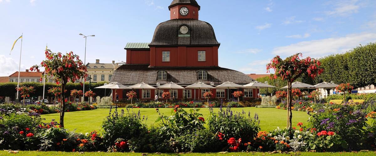 A red church with a clock tower, surrounded by a well-maintained garden with various flowers and trees.