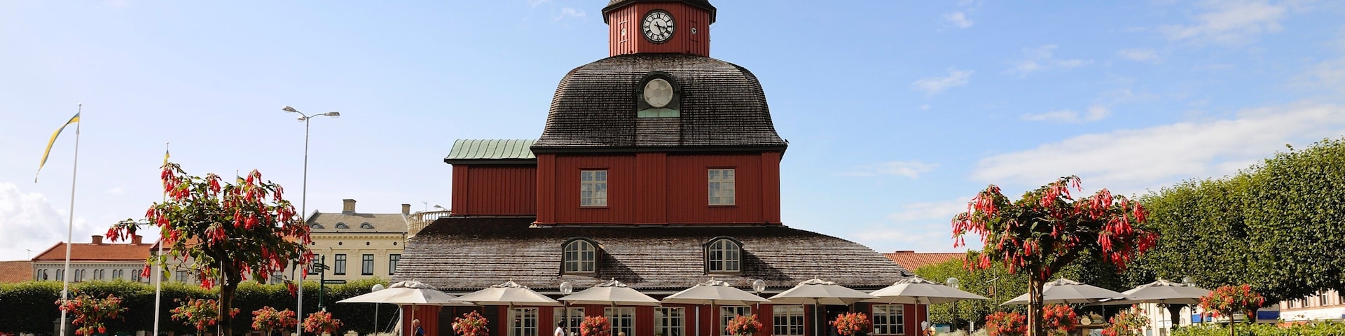 A red church with a clock tower, surrounded by a well-maintained garden with various flowers and trees.