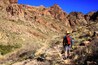 Un randonneur sur un sentier rocailleux, avec des montagnes en arrière-plan.