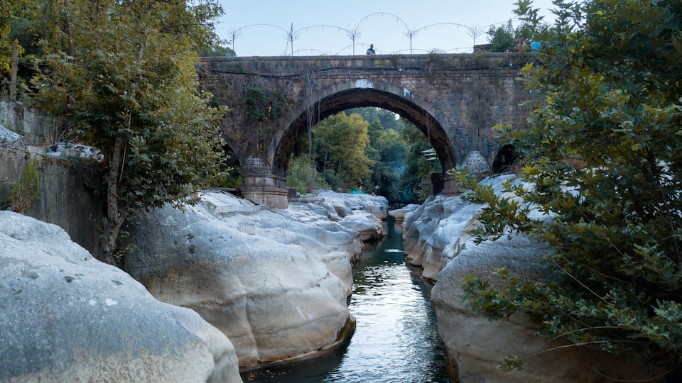 A stone bridge over a narrow water channel, surrounded by large boulders and trees.