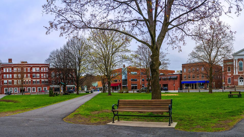 A park with a bench, a path, and a historic building with a clock tower.