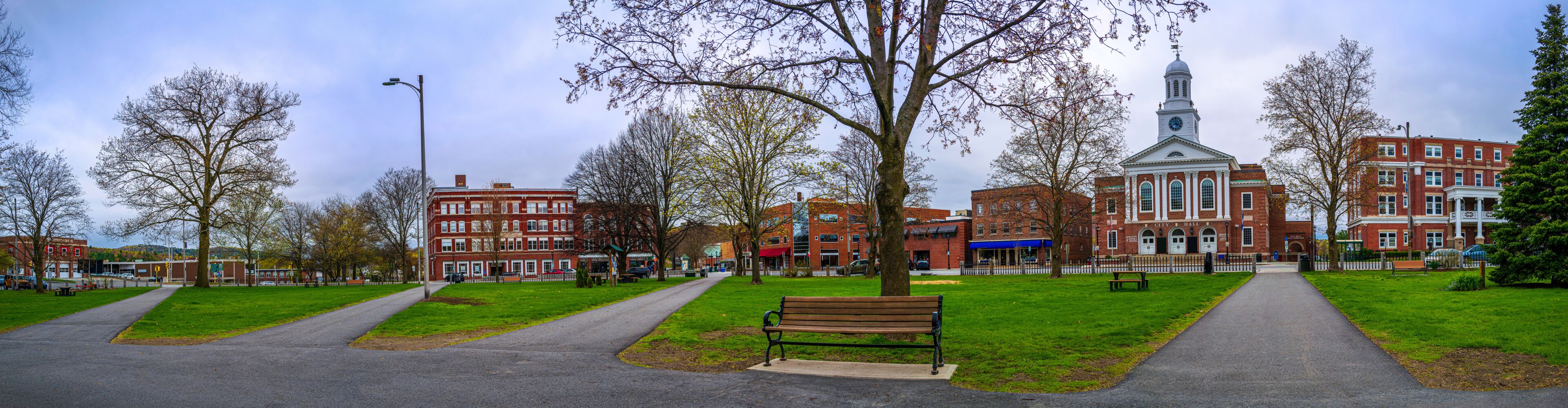 A park with a bench, a path, and a historic building with a clock tower.