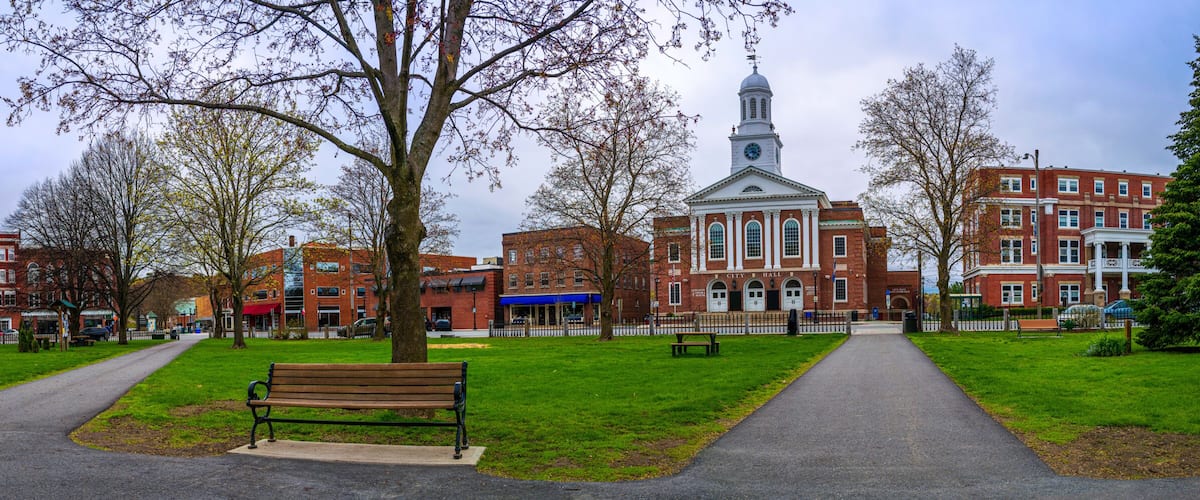 A park with a bench, a path, and a historic building with a clock tower.