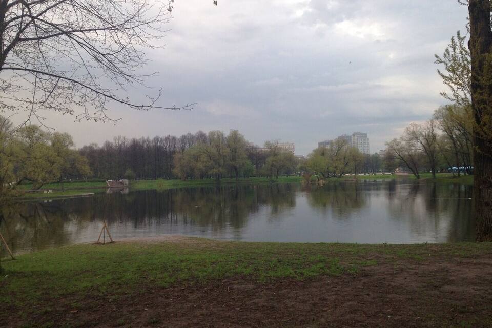 A park with a lake, trees, and a distant building.