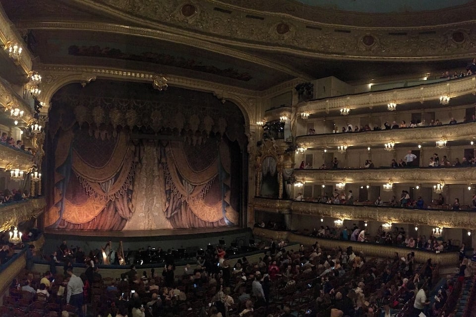 A grand opera house interior with ornate chandeliers, tiered balconies, and a large stage.