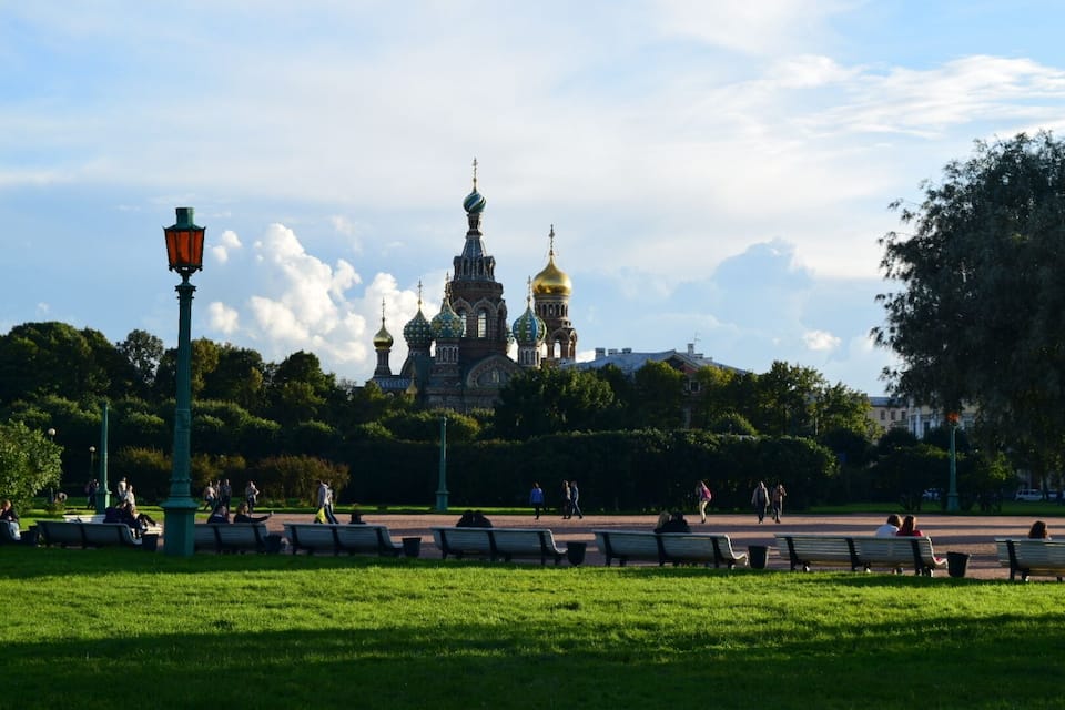 A park with benches, a large ornate building with golden domes, and a clear sky.
