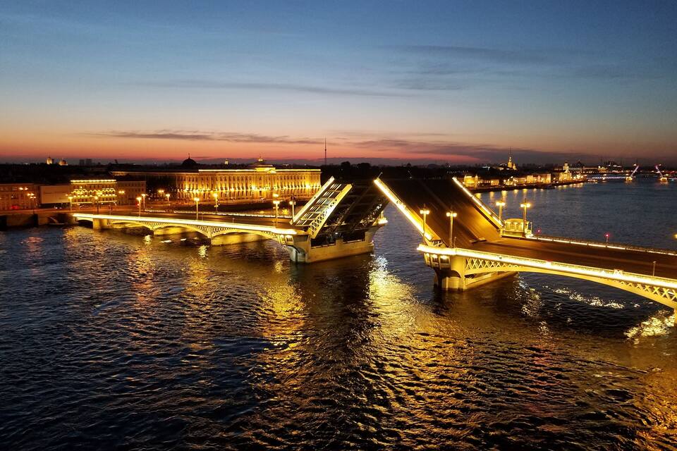 Un pont illuminé dont les lumières se reflètent sur l’eau au crépuscule.