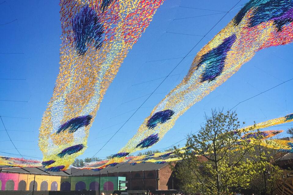 Une foule nombreuse se promène sur un chemin pavé, au-dessus duquel sont installées des décorations lumineuses aux couleurs vives.