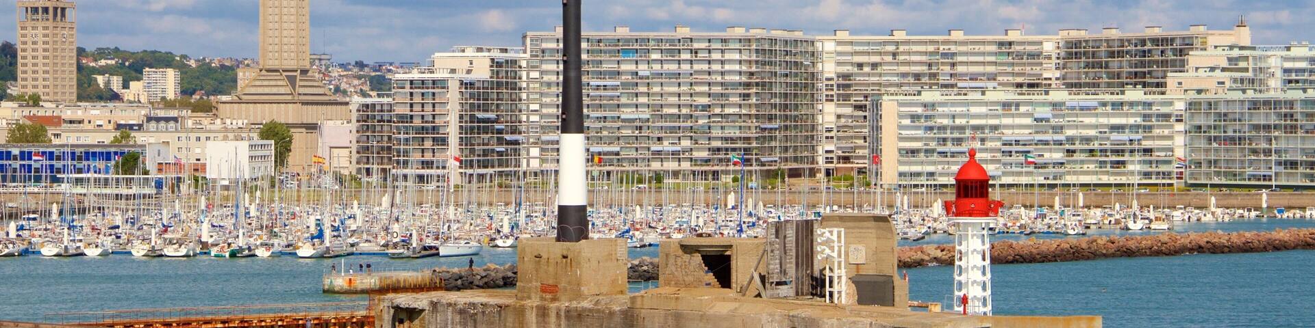 A harbor with a lighthouse, a large building, and a tower in the background.