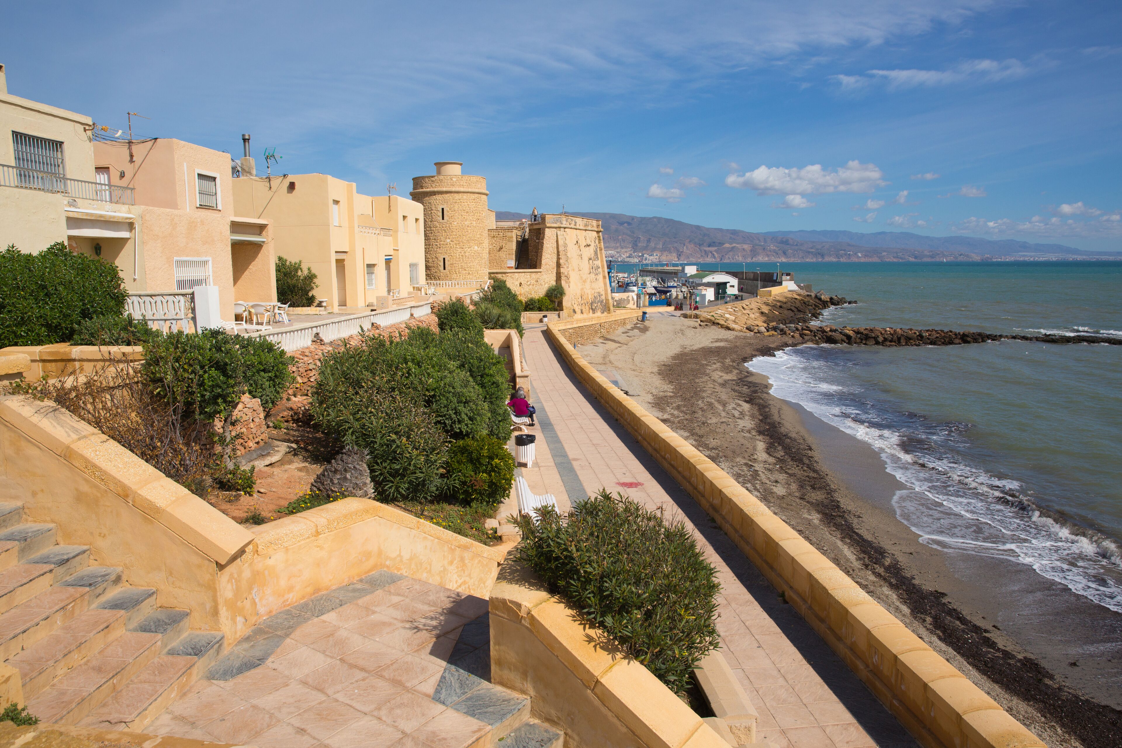 A coastal promenade with a stone staircase, a sea wall, and a historic tower.